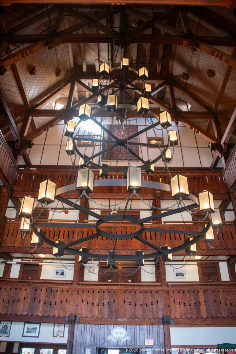 Two enormous circular chandeliers suspended beneath timber roof trusses above carved lobby balconies.