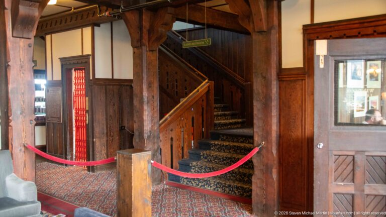 Carpeted wooden staircase with carved railing and heavy posts, cordoned by red ropes inside the hotel.
