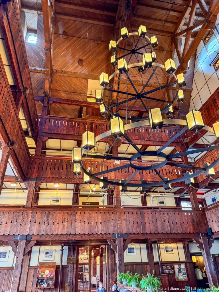 Several large circular chandeliers overlap beneath a timber ceiling and carved upper balconies in the hotel lobby.