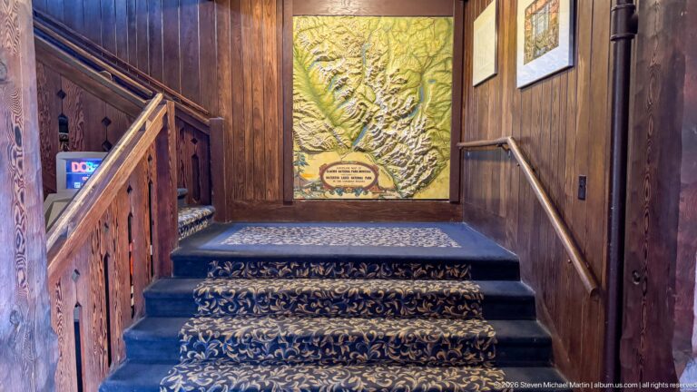 Raised terrain map mounted above a short carpeted staircase with dark wooden railings and paneled walls.