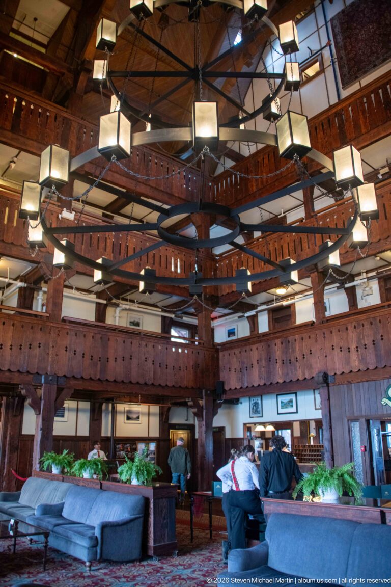 Multi-story timber hotel lobby with balconies, geometric hanging lights, seating, and exposed roof framing.