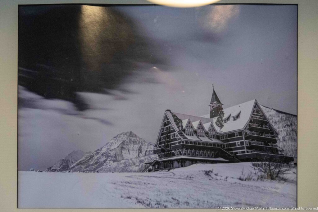 Framed black-and-white winter view of the Prince of Wales Hotel surrounded by deep snow and mountains.