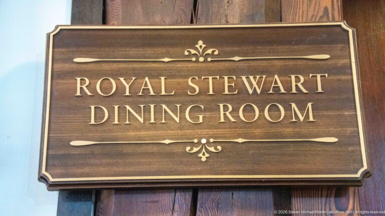 Dark wooden plaque with gold lettering reading Royal Stewart Dining Room and small decorative flourishes.