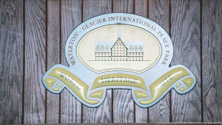 Round Waterton-Glacier International Peace Park emblem with stylized hotel and World Heritage Site ribbon on wood paneling.