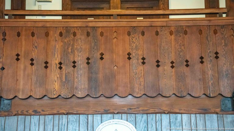 Close view of stained wooden balcony boards with diamond cutouts and a scalloped lower edge.