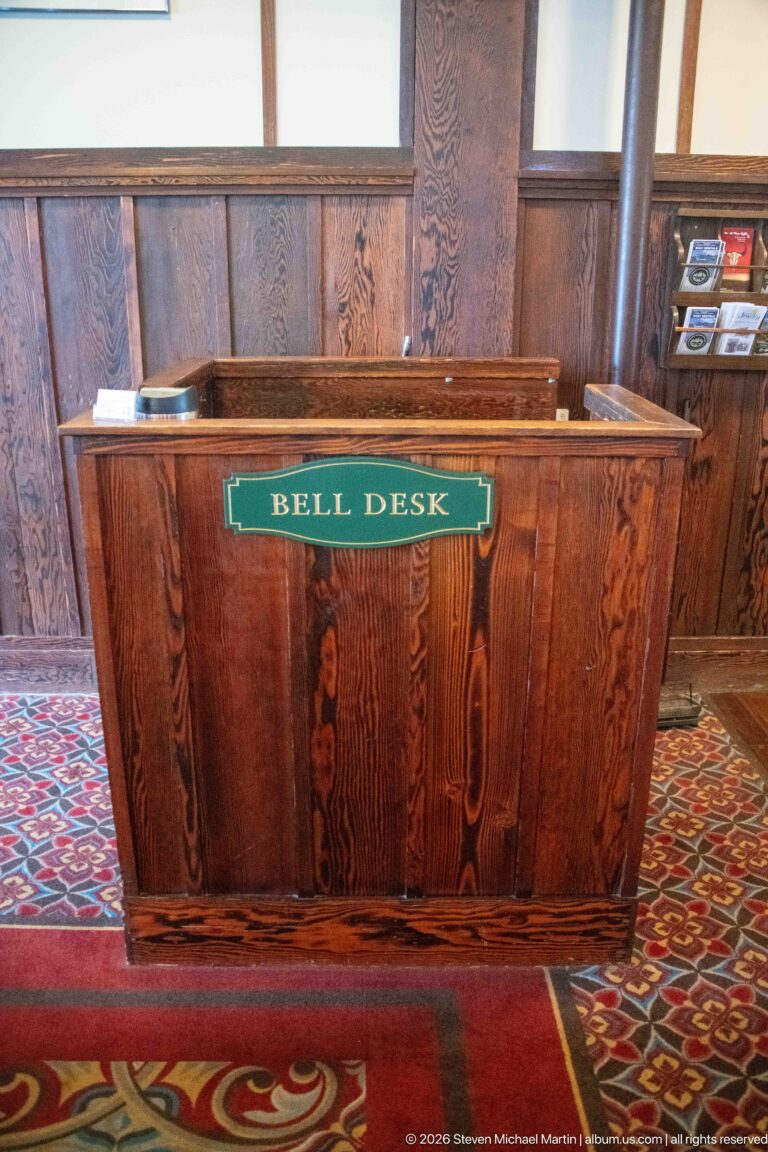 Small paneled wooden desk with a green sign reading Bell Desk, standing on patterned carpet.