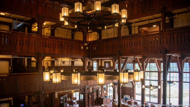 Multi-story hotel lobby with dark timber balconies and several glowing geometric chandeliers.