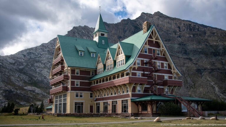 Prince of Wales Hotel with stacked balconies and steep green roofs set against a gray rocky mountain.