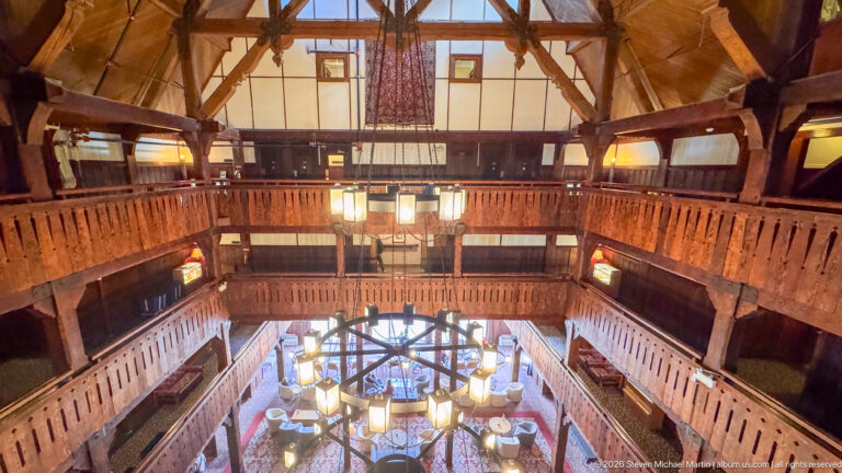 Upper lobby view with stacked carved-wood balconies, exposed roof structure, and a large circular chandelier below.