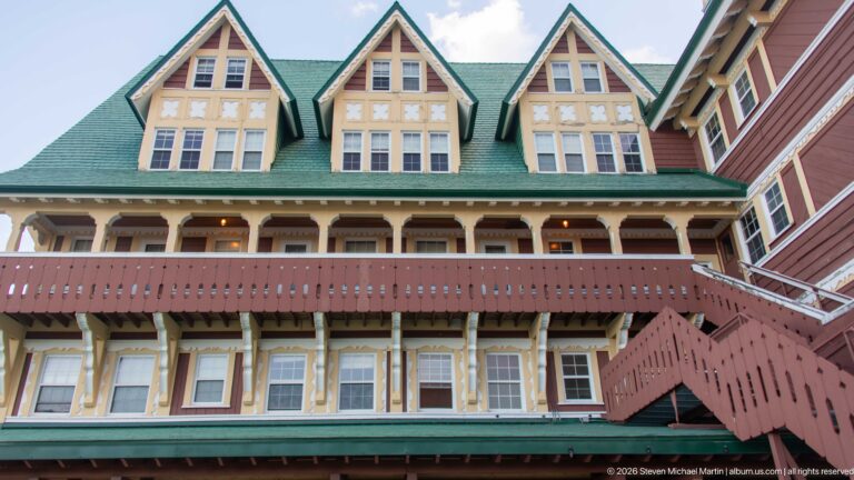 Prince of Wales Hotel façade with three steep dormer gables, green roof, veranda, pierced balcony rail, and exterior stair.